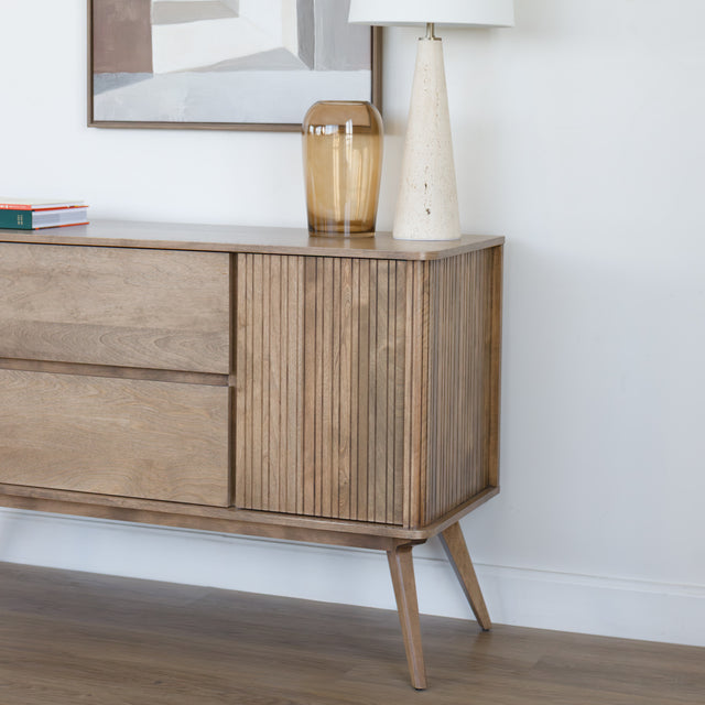 Buffet en bois clair style scandinave avec portes rainurées, pieds inclinés et déco minimaliste dans un salon moderne.
