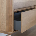 Buffet bas en bois clair avec tiroirs et porte rainurée, design scandinave sur pieds compas dans un intérieur épuré.