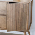 Buffet bas en bois clair avec tiroirs et porte rainurée, design scandinave sur pieds compas dans un intérieur épuré.