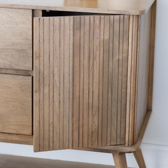 Buffet bas en bois clair avec tiroirs et porte rainurée, design scandinave sur pieds compas dans un intérieur épuré.