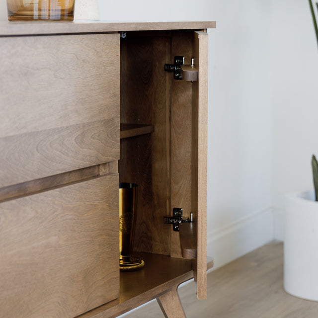 Buffet bas en bois clair avec tiroirs et porte rainurée, design scandinave sur pieds compas dans un intérieur épuré.