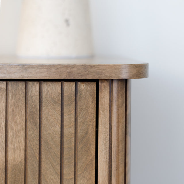 Buffet bas en bois clair avec tiroirs et porte rainurée, design scandinave sur pieds compas dans un intérieur épuré.