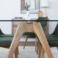 Table à manger en verre avec pieds en bois et chaises en tissu vert, style moderne dans un intérieur lumineux.