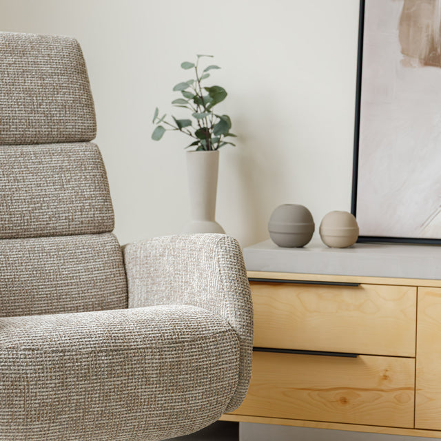 Fauteuil en tissu beige avec dossier inclinable et base pivotante, dans un salon lumineux et épuré.
