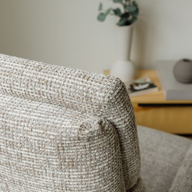 Fauteuil en tissu beige avec dossier inclinable et base pivotante, dans un salon lumineux et épuré.