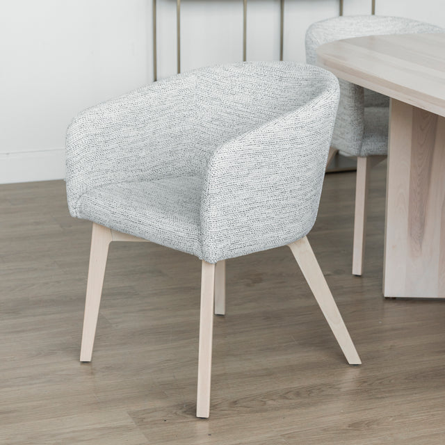 Chaise moderne en tissu crème avec pieds en bois clair dans une salle a manger minimaliste.
