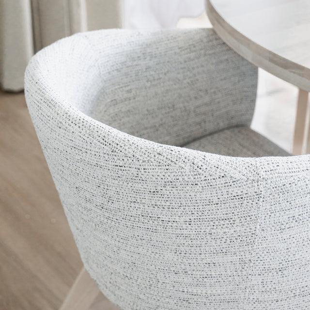 Image rapprochée d'une chaise moderne en tissu crème avec pieds en bois clair dans une salle a manger minimaliste.