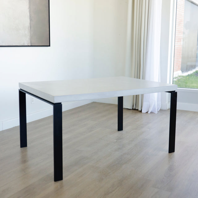 Table rectangulaire moderne avec plateau en béton gris clair et pieds metalliques noirs.