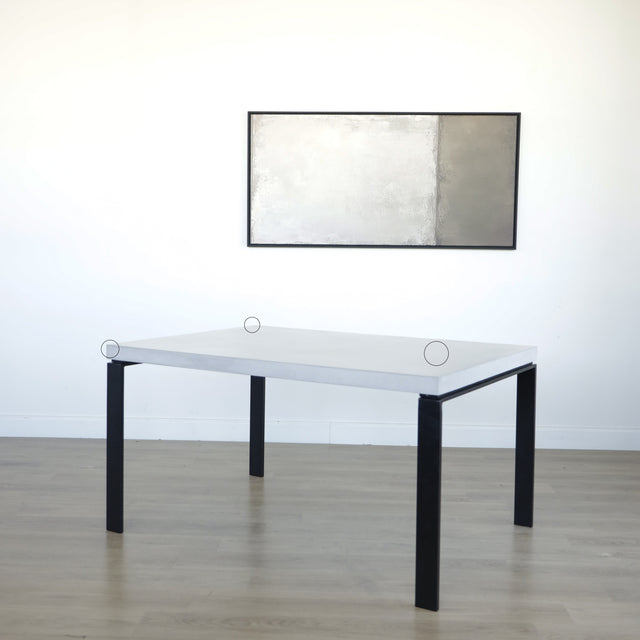 Table rectangulaire moderne avec plateau en béton gris clair et pieds metalliques noirs avec cercles indiquant les défauts.