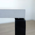 Image rapprochée d'une Table rectangulaire moderne avec plateau en béton gris clair et pieds metalliques noirs.