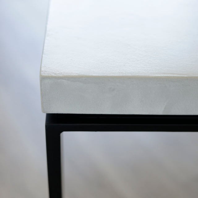 Image rapprochée d'une Table rectangulaire moderne avec plateau en béton gris clair et pieds metalliques noirs.