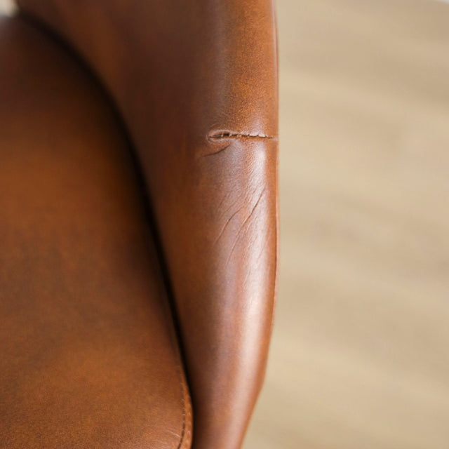Image rapprochée d'une chaise moderne en cuir cognac avec dossier incurvé et pieds noirs élegants.
