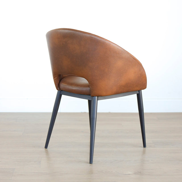 Chaise moderne en cuir cognac avec dossier incurvé et pieds noirs élegants.