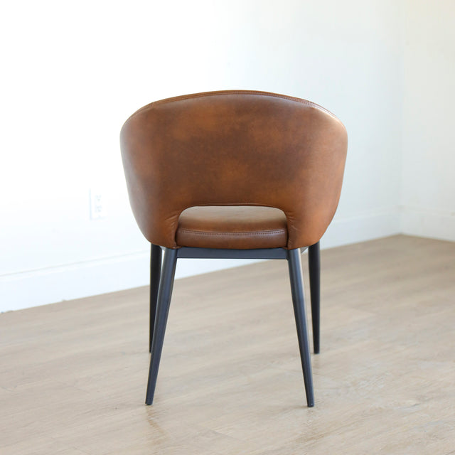Chaise moderne en cuir cognac avec dossier incurvé et pieds noirs élegants.