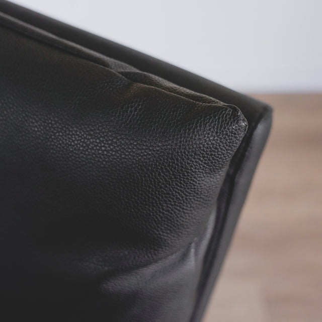 image rapprochée d'une chaise en cuir noir avec coussins rembourrés et pieds en bois sombre.