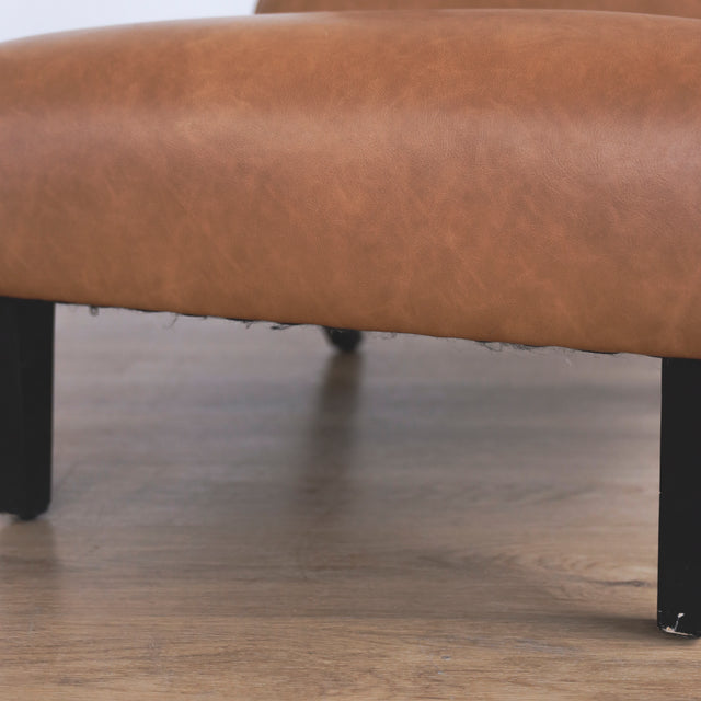 Image rapprochée d'un fauteuil moderne en cuir végane cognac avec pieds noirs sur sol en bois.