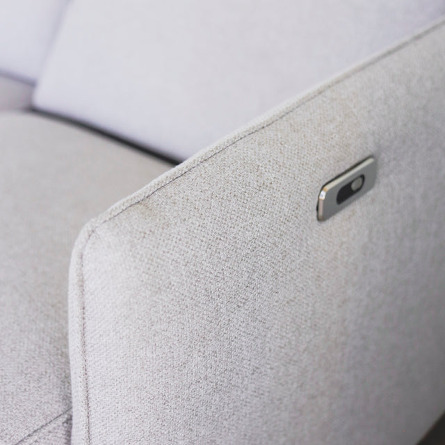 detail du bouton metalique sur accoudoir de canape gris clair en tissu moderne.
