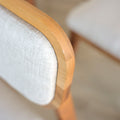image rapprochée d'une chaise en bois de noyer avec assise et dossier rembourres en tissu beige.