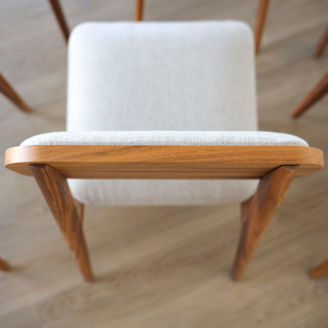 image rapprochée d'une chaise en bois de noyer avec assise et dossier rembourres en tissu beige.