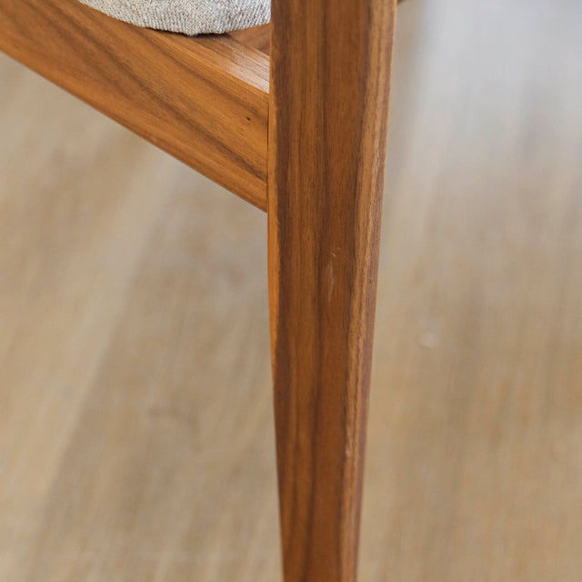 image rapprochée d'une chaise en bois de noyer avec assise et dossier rembourres en tissu beige.