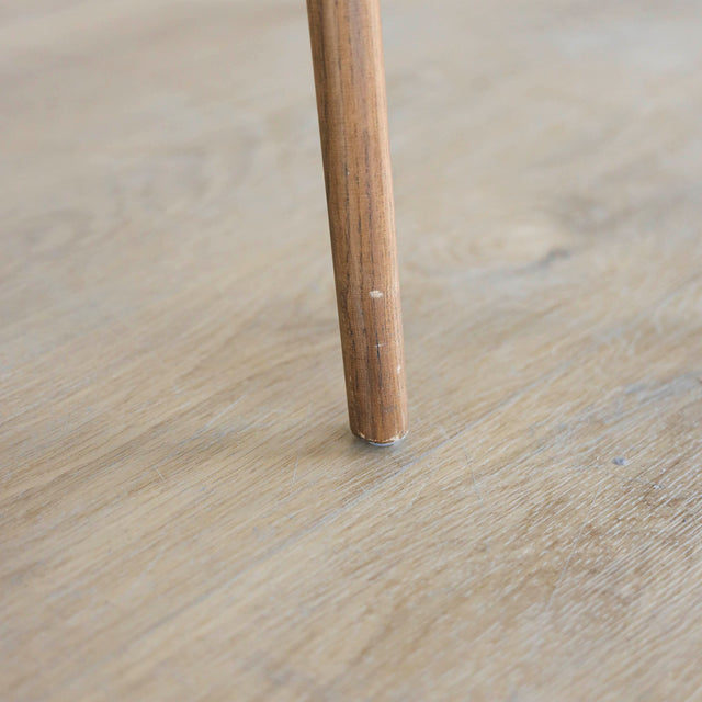 Image rapprochée d'une patte en bois d'un lot de trois chaises style scandinave avec structure en bois et assise beige rembourree.