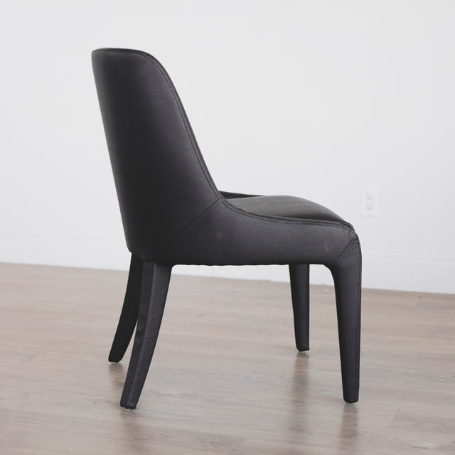 chaise contemporaine en cuir végane noir avec design incurve et pieds assortis.