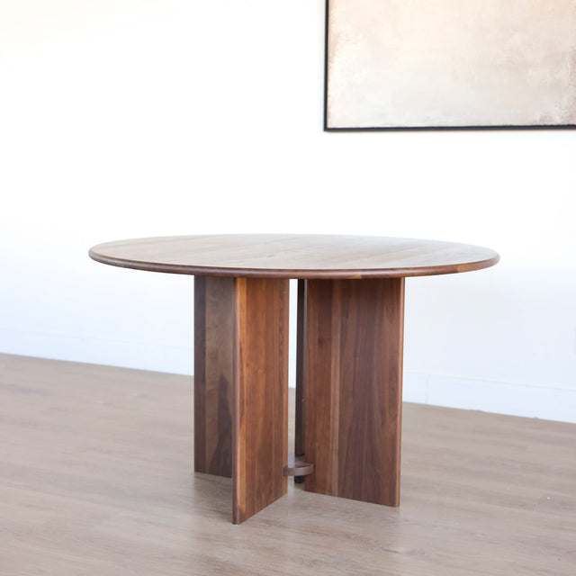 Table ronde en noyer massif avec pied central croise au design contemporain.
