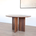 Table ronde en noyer massif avec pied central croise au design contemporain.