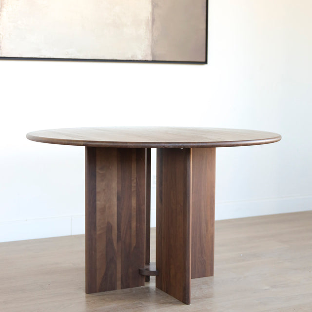 Table ronde en noyer massif avec pied central croise au design contemporain.