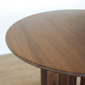 Table ronde en noyer massif avec pied central croise au design contemporain.