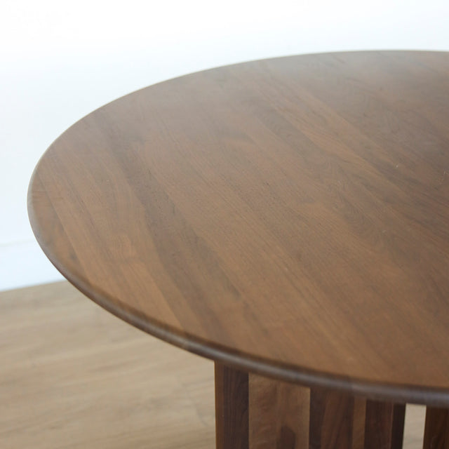 Table ronde en noyer massif avec pied central croise au design contemporain.
