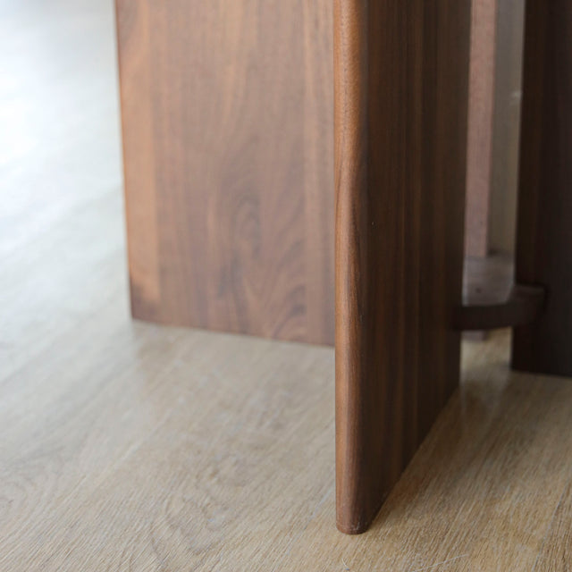 Image rapprochée du piétement d'une table ronde en noyer massif avec pied central croise au design contemporain.