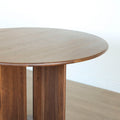 Table ronde en noyer massif avec pied central croise au design contemporain.