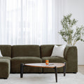 Sectionnel en tissu vert olive avec méridienne gauche, au design arrondi et contemporain dans un salon lumineux.