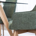 Chaise de salle à manger en tissu vert avec accoudoirs et pieds en bois, style moderne autour d’une table en verre.