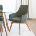 Chaise de salle à manger en tissu vert avec accoudoirs et pieds en bois, style moderne autour d’une table en verre.