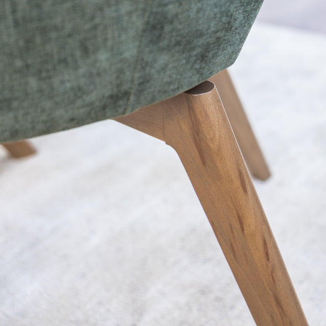Chaise de salle à manger en tissu vert avec accoudoirs et pieds en bois, style moderne autour d’une table en verre.