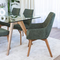 Chaise de salle à manger en tissu vert avec accoudoirs et pieds en bois, style moderne autour d’une table en verre.