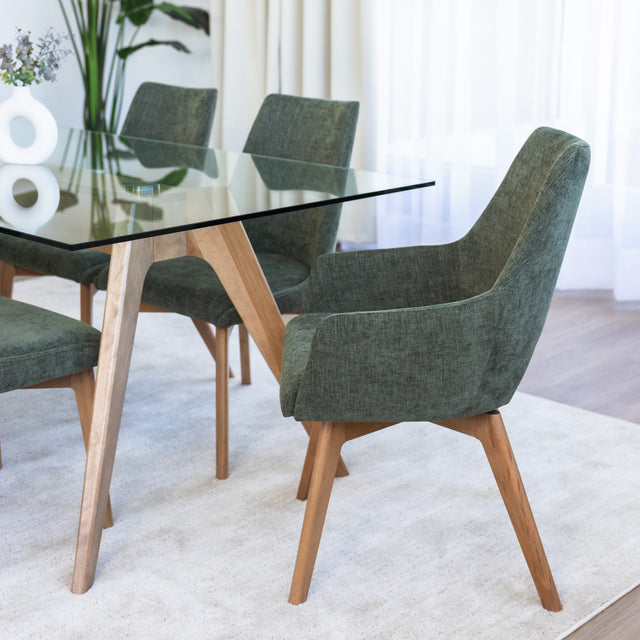 Chaise de salle à manger en tissu vert avec accoudoirs et pieds en bois, style moderne autour d’une table en verre.