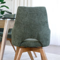 Chaise de salle à manger en tissu vert avec accoudoirs et pieds en bois, style moderne autour d’une table en verre.