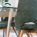 Chaise de salle à manger en tissu vert avec accoudoirs et pieds en bois, style moderne autour d’une table en verre.