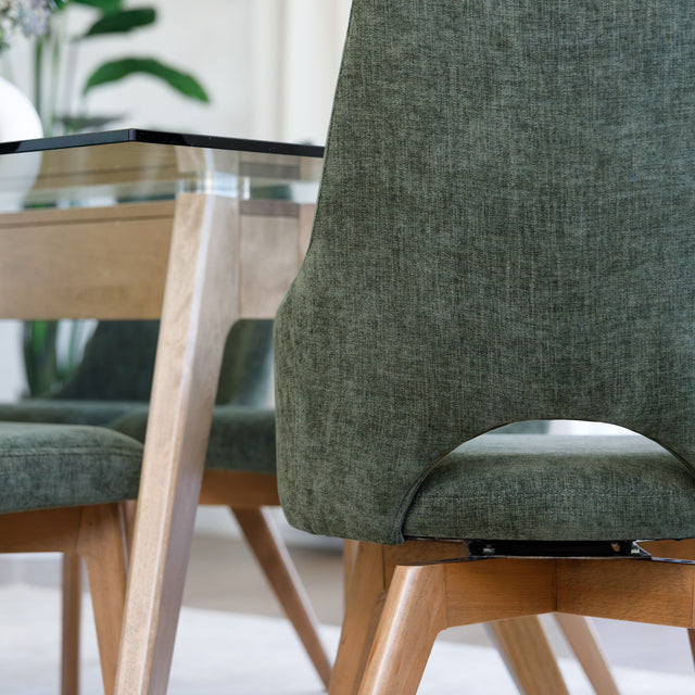 Chaise de salle à manger en tissu vert avec accoudoirs et pieds en bois, style moderne autour d’une table en verre.