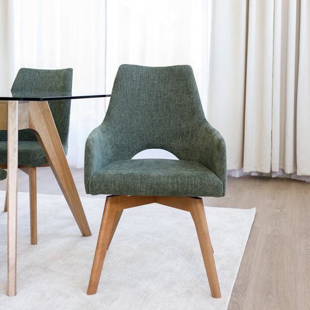 Chaise de salle à manger en tissu vert avec accoudoirs et pieds en bois, style moderne autour d’une table en verre.