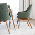 Chaise de salle à manger en tissu vert avec accoudoirs et pieds en bois, style moderne autour d’une table en verre.
