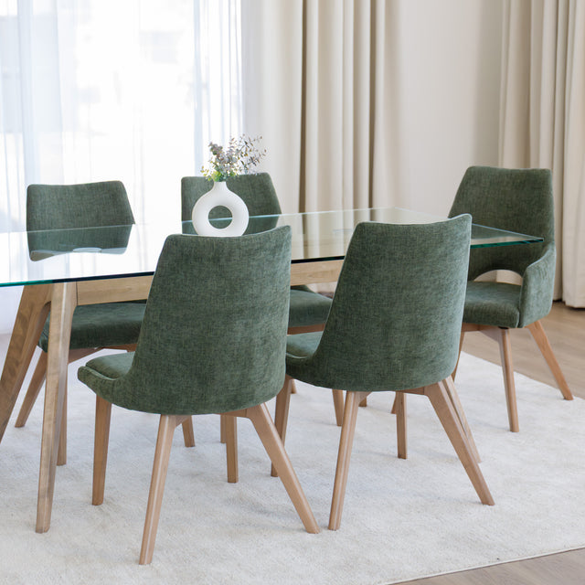 Chaise de salle à manger en tissu vert avec accoudoirs et pieds en bois, style moderne autour d’une table en verre.