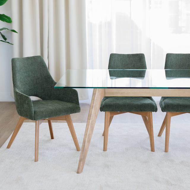 Chaise de salle à manger en tissu vert avec accoudoirs et pieds en bois, style moderne autour d’une table en verre.