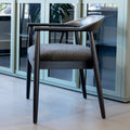 Chaise de salle à manger contemporaine avec accoudoirs noirs et assise rembourrée en tissu texturé gris.