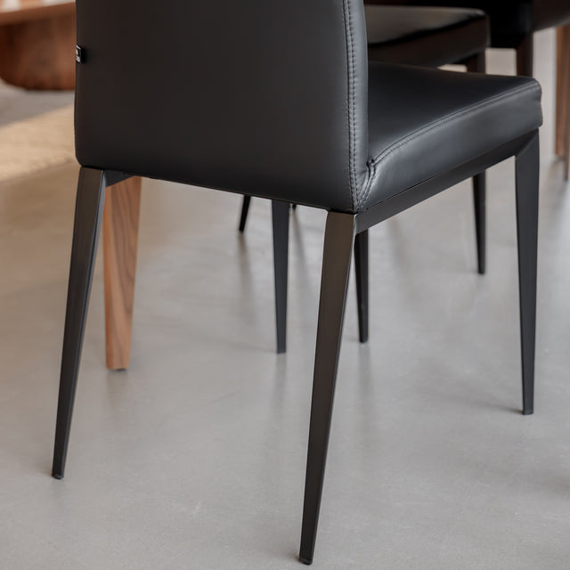 Chaise de salle à manger en cuir noire avec pieds fins, placée autour d’une table en bois massif moderne.