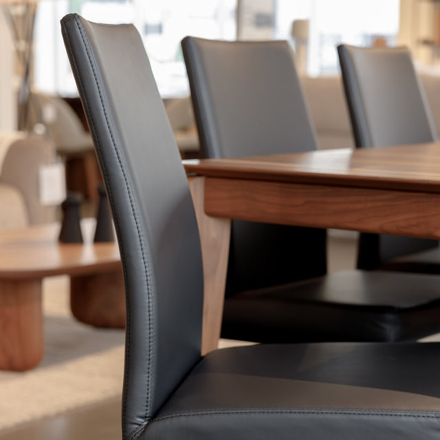Chaise de salle à manger en cuir noire avec pieds fins, placée autour d’une table en bois massif moderne.