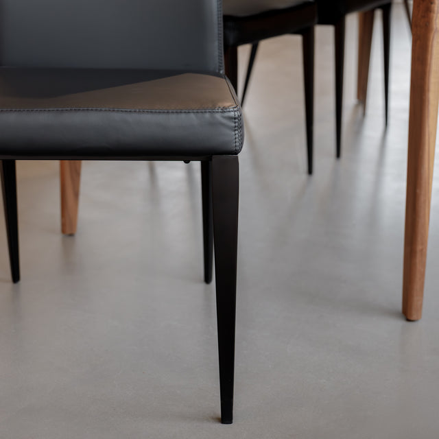 Chaise de salle à manger en cuir noire avec pieds fins, placée autour d’une table en bois massif moderne.
